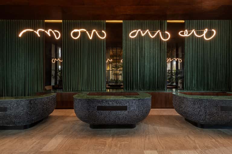 Modern building entrance with glowing neon signage on dark corrugated metal facade and stone planter features
