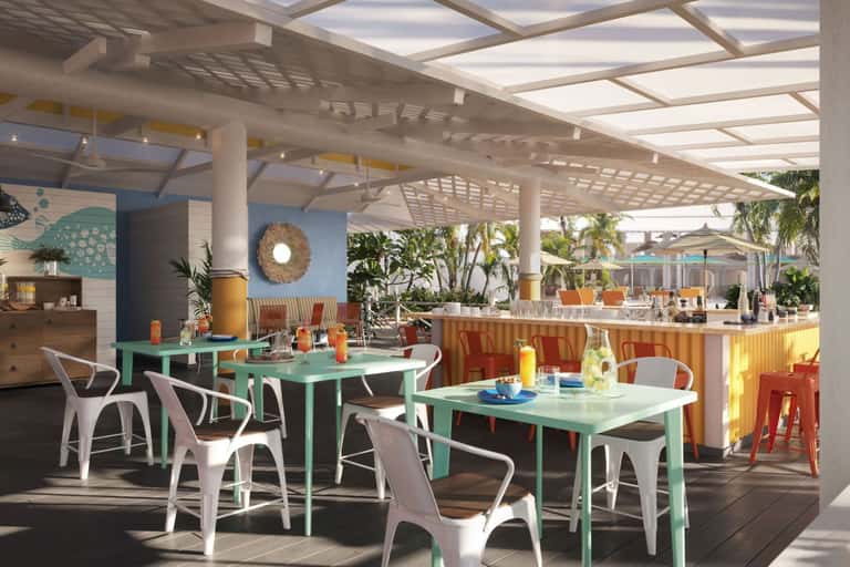 Beachfront outdoor dining pavilion with mint green tables, white chairs, yellow umbrellas, and ocean views