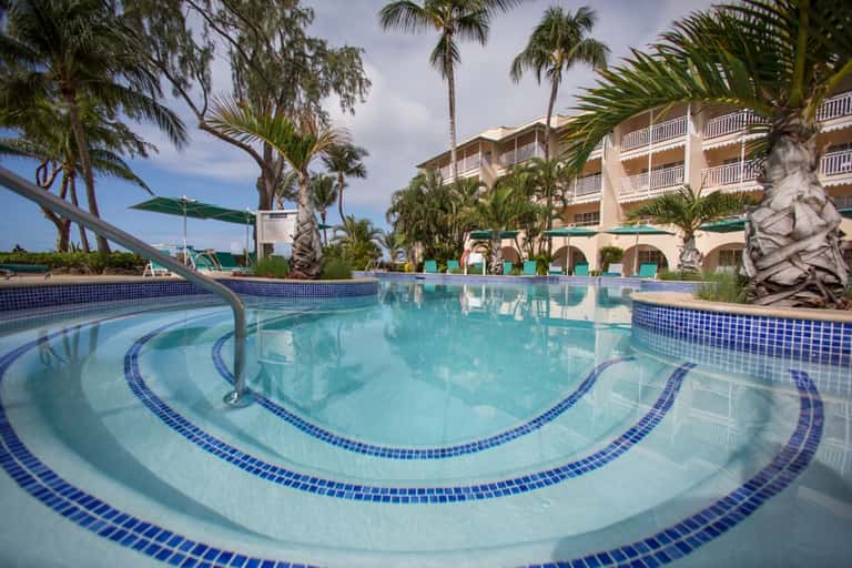 Resort swimming pool with decorative tile patterns, palm trees, multi-story hotel building, and lounge chairs