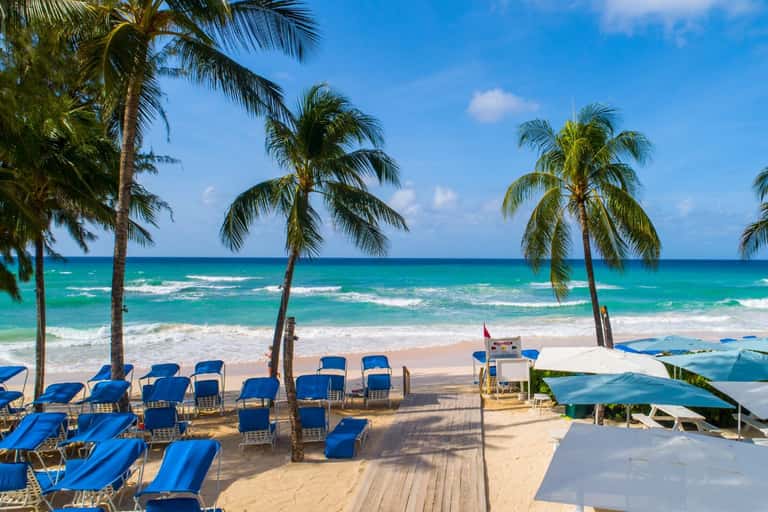 Beach club with blue lounge chairs, palm trees, white umbrellas, turquoise ocean, white sand, and beach bar