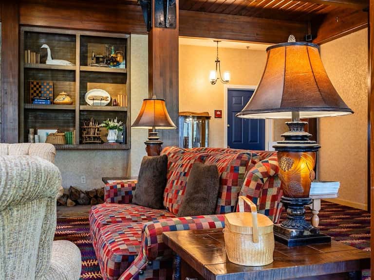 Cozy living room with wood ceiling, plaid furniture, amber lamps, and built-in shelving