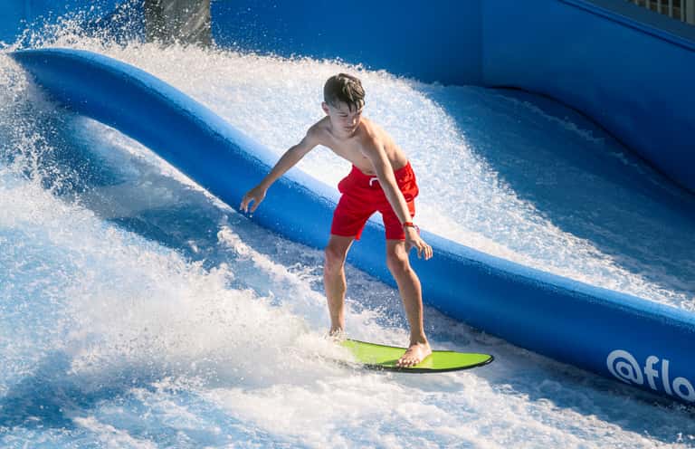 Boy surfing on a green board down a blue FlowRider artificial wave machine