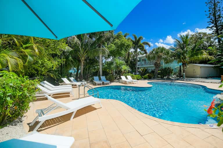 Resort swimming pool with turquoise water, lounge chairs, and tropical palm trees under blue sky