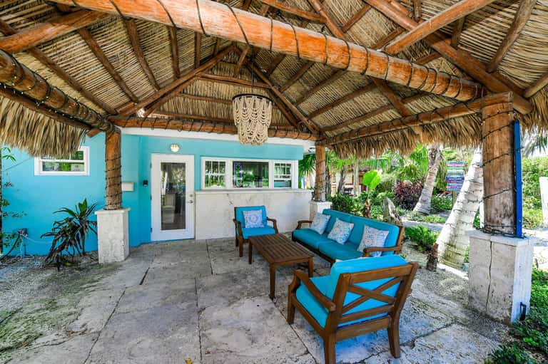Beachfront tiki bar with turquoise walls, wooden furniture, and thatched roof canopy