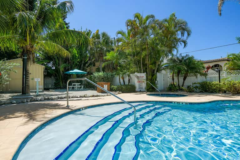 Swimming pool with blue lane markers, metal handrail, palm trees, and sandy deck area