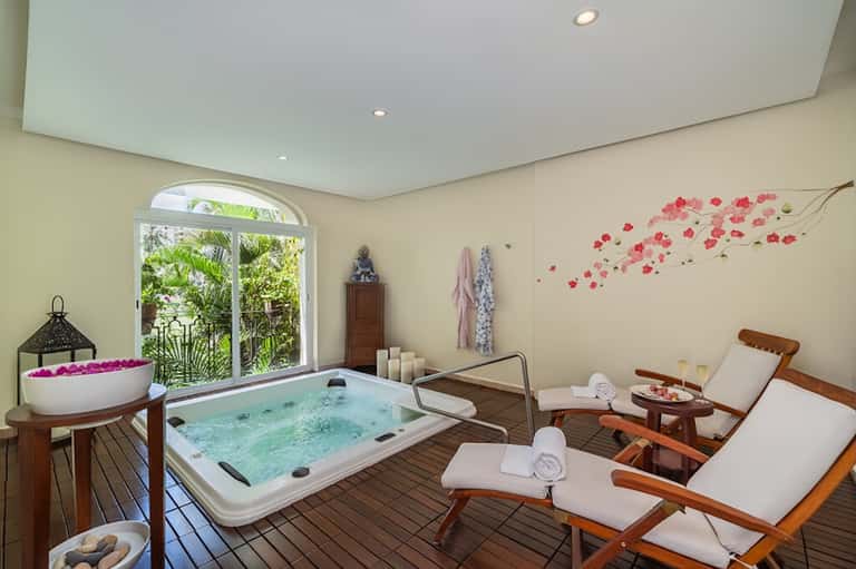 Spa relaxation area with hot tub, massage beds, flowers, and garden view through glass doors