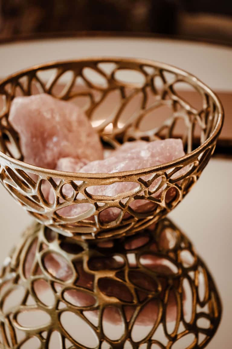 Decorative gold filigree bowl with pink rose petals on white surface