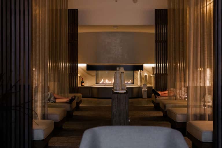 Spa relaxation room with fireplace, golden curtains, and cushioned seating areas