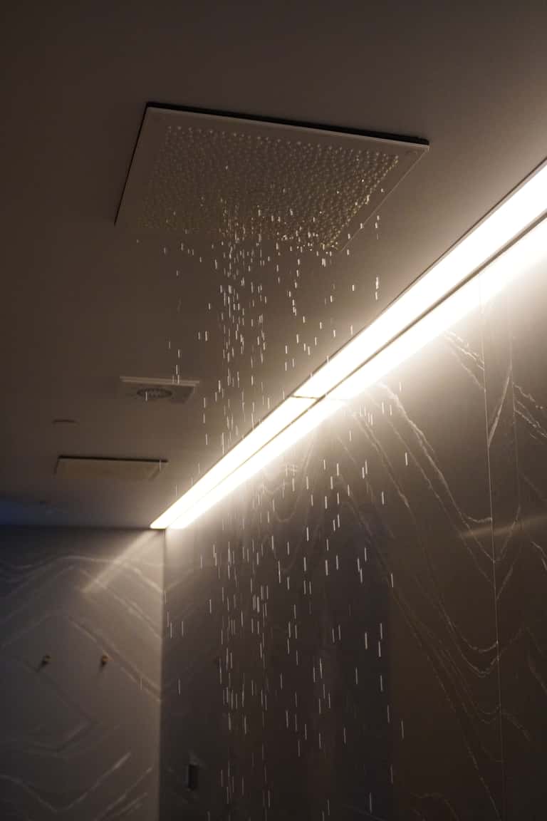 Luxury rainfall showerhead with water streaming down, illuminated by warm LED lighting and marble surroundings