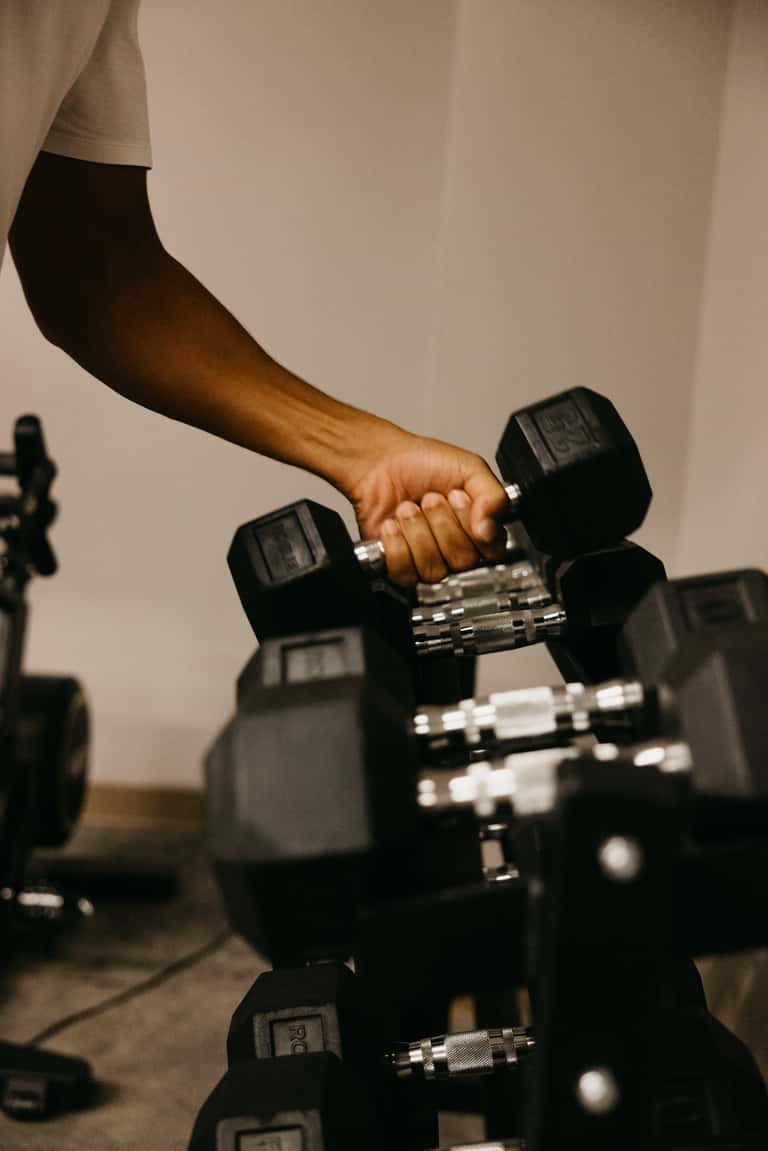 Close-up of person's arm lifting black dumbbell from gym weight rack with dumbbells on floor