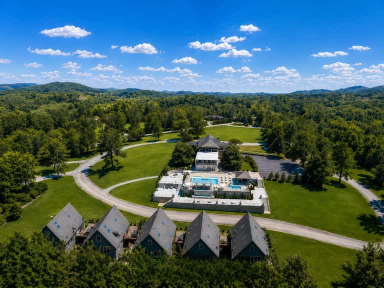 Aerial view of resort property with pools, guest cottages, and forested landscape