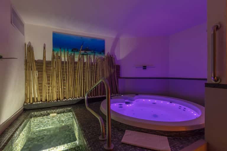 Spa relaxation area with purple-lit jacuzzi, bamboo accents, and decorative pool featuring underwater lighting