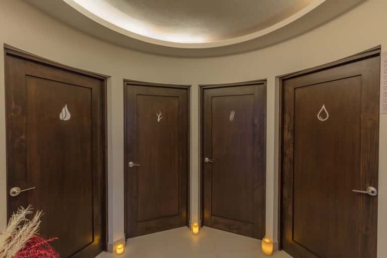 Four dark wooden spa treatment room doors with elemental icons: flame, leaf, steam, and water droplet
