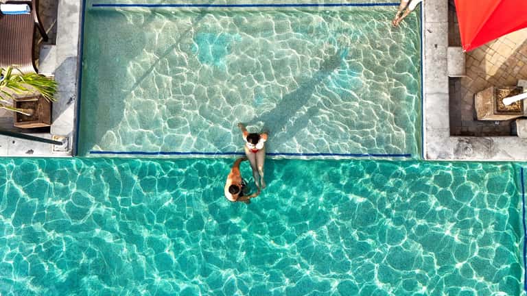 Overhead view of couple swimming in crystal-clear turquoise resort pool