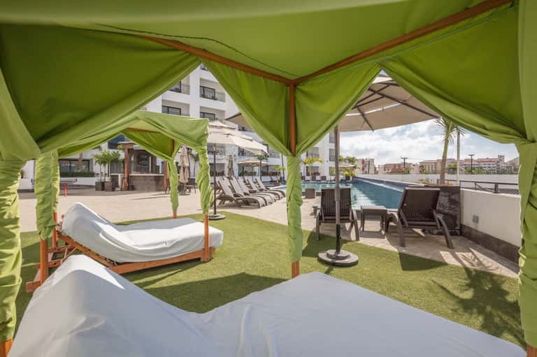 Luxury poolside cabanas with green curtains, white daybeds, and lounge seating overlooking the pool area