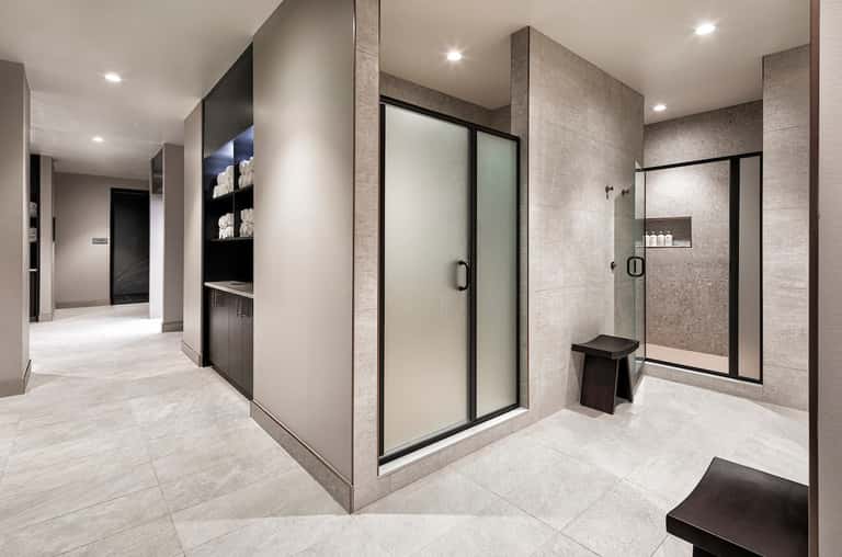 Modern spa bathroom with dual walk-in showers, stone tile walls, recessed lighting, and minimalist design