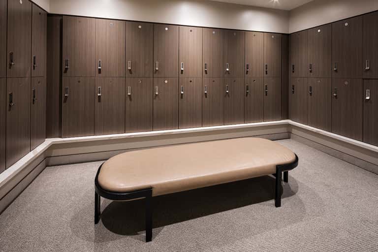 Modern locker room with dark wood cabinetry, white trim, gray carpet, and a tan leather bench in center