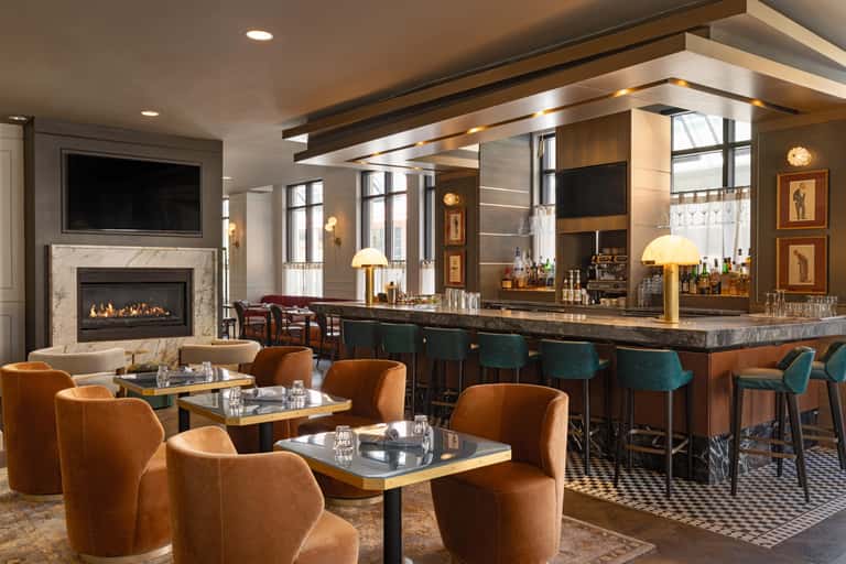 Upscale hotel bar and lounge with fireplace, orange velvet seating, dark wood accents, and marble countertop