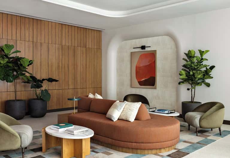 Contemporary lounge with rust-colored curved sofa, wooden wall paneling, potted plants, and abstract artwork
