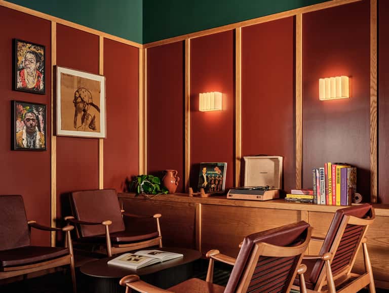 Sophisticated lounge with terracotta walls, wooden paneling, vintage furniture, artwork, and warm ambient lighting