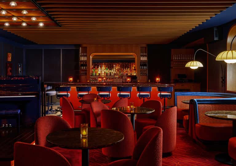 Upscale bar lounge featuring red seating, wooden ceiling, illuminated bar counter, and entertainment amenities