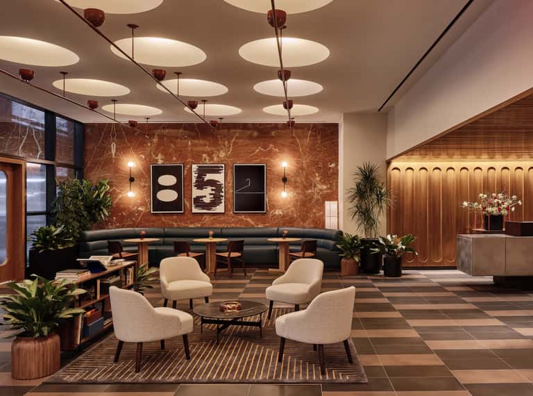 Modern hotel lobby with warm tones, circular seating arrangement, marble accent wall, pendant lighting, and contemporary art