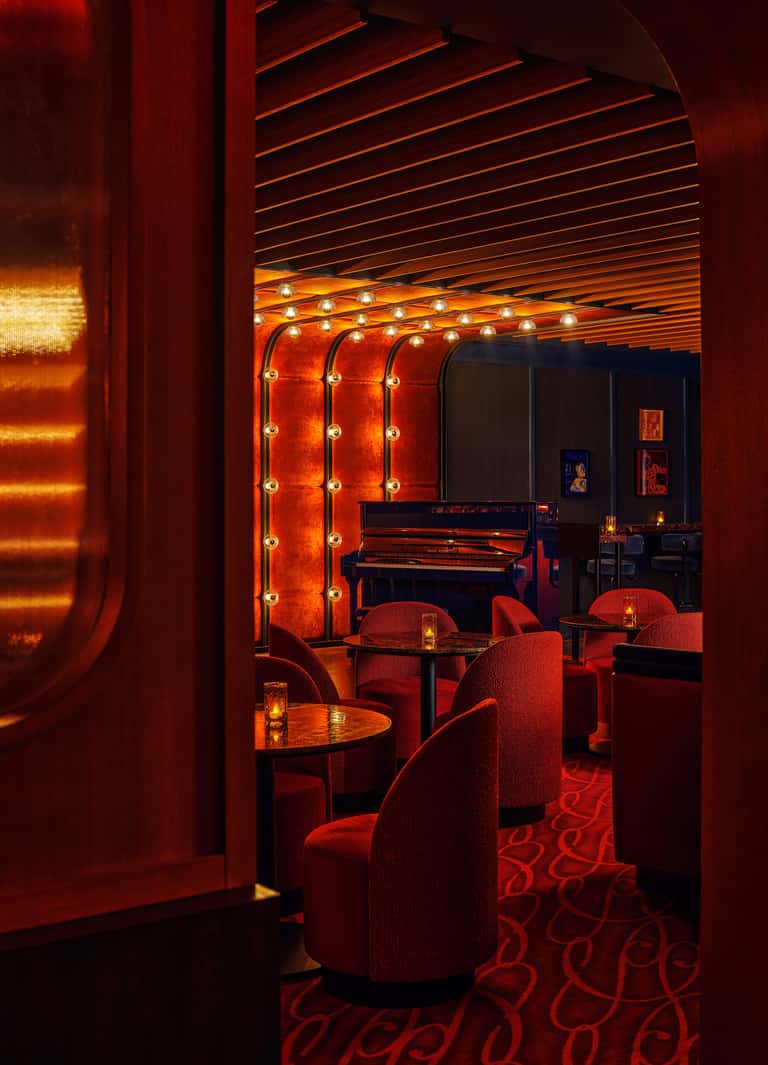 Intimate red-themed music lounge with marquee lighting, grand piano, and plush seating