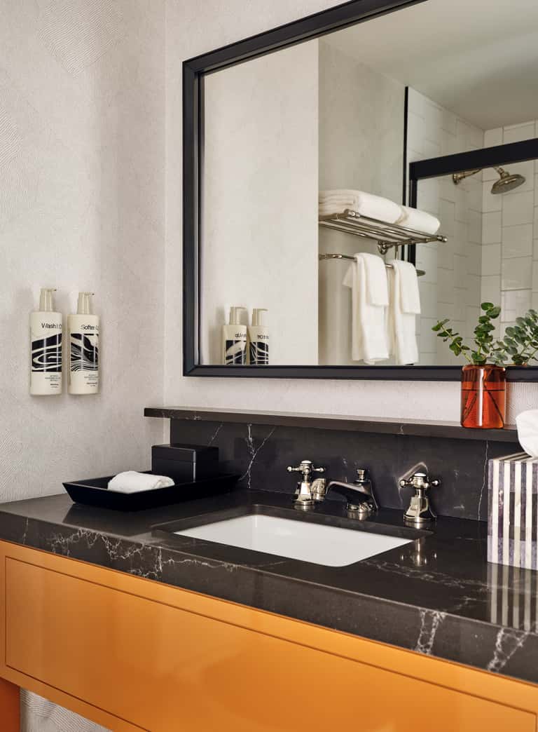 Luxury bathroom vanity with black marble countertop, framed mirror, and orange cabinet base