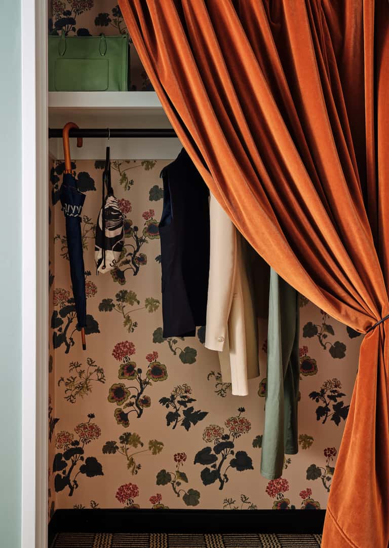 Chic closet interior with floral wallpaper, shelving, and flowing orange drapery panel