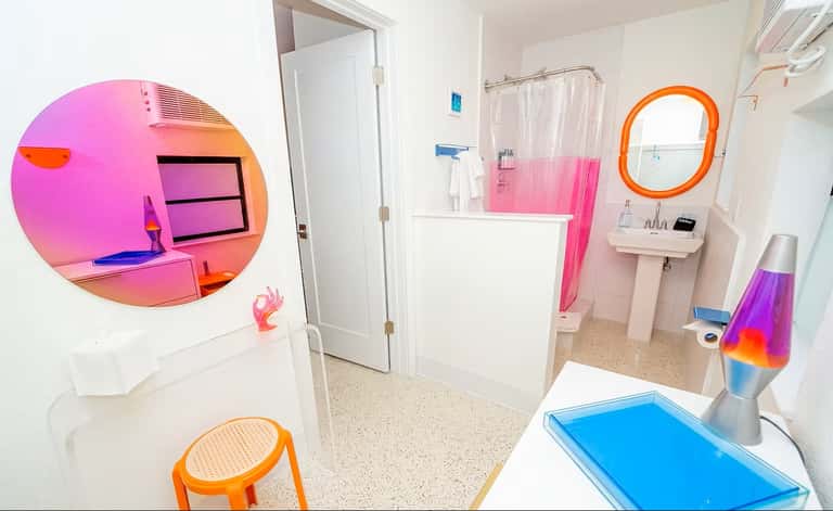 Colorful bathroom with pink shower curtain, orange circular mirror, neon pink circular wall art, and blue lava lamp decoration
