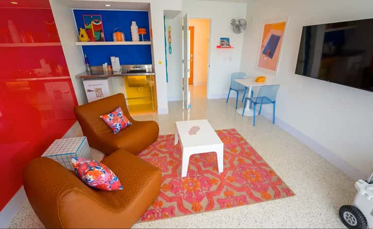 Contemporary family lounge with brown leather seating, red accent wall, blue shelving, colorful rug, and flat-screen TV