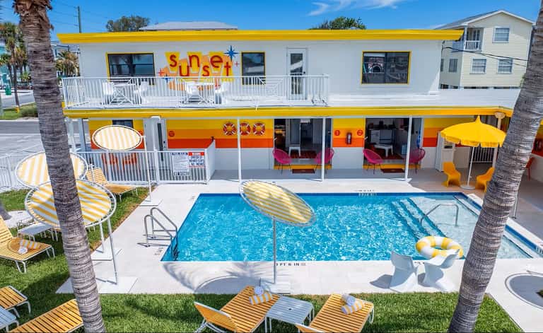 Retro-style motel with bright yellow trim, pink seating visible through windows, and rectangular pool with loungers
