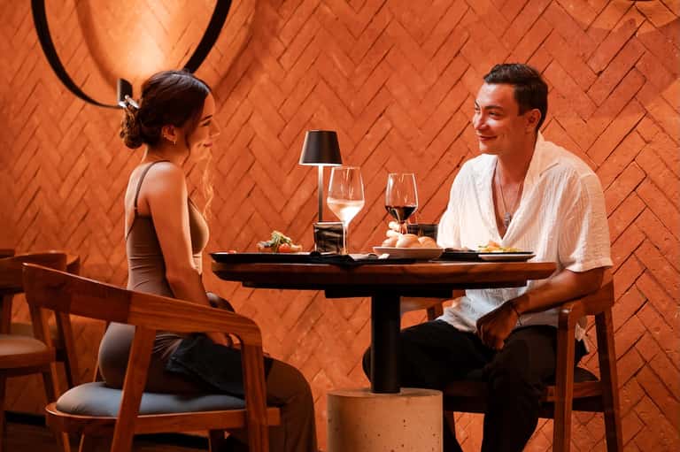 Couple dining together at an intimate table in a warm orange-brick restaurant with wine glasses and plated dishes