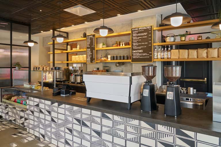 Contemporary coffee shop interior with concrete walls, wooden shelving, white counter, pendant lighting, and organized merchandise displays