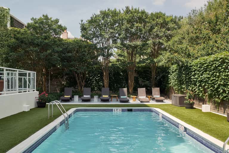Residential backyard with rectangular swimming pool, lounge chairs, mature trees, ivy-covered walls, and manicured lawn