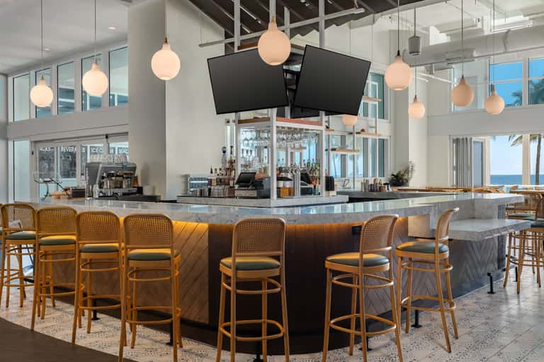 Modern hotel bar with pendant lighting, ocean views, and wood accent seating