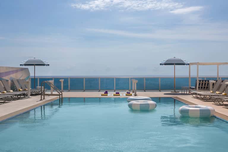 Resort rooftop pool with striped umbrellas, loungers, and ocean horizon views
