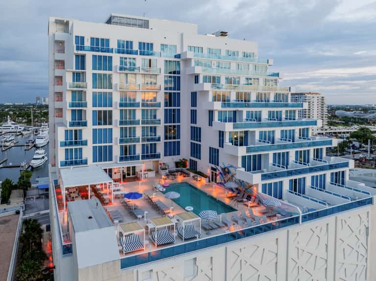 Modern beachfront hotel at dusk with lit pool deck and waterfront balconies