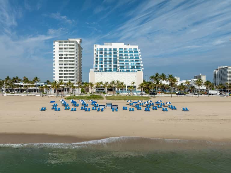 Aerial view of beachfront resort with blue umbrellas and guest gathering spaces