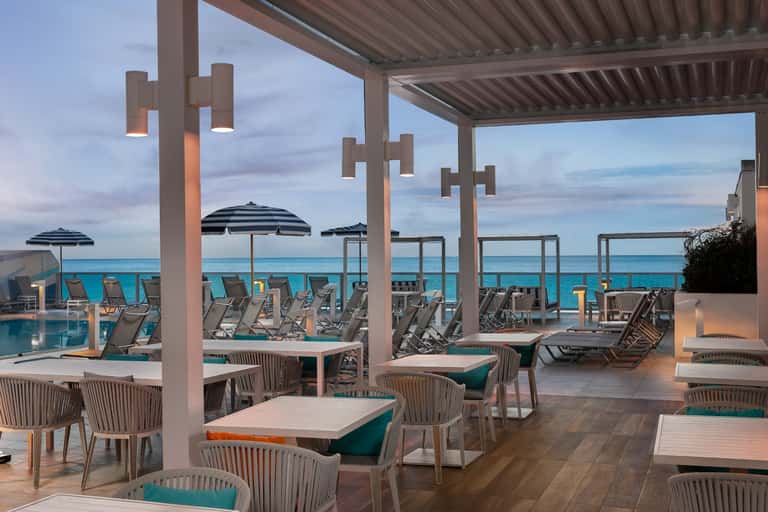 Waterfront dining terrace with striped umbrellas, lounge chairs, and turquoise ocean view