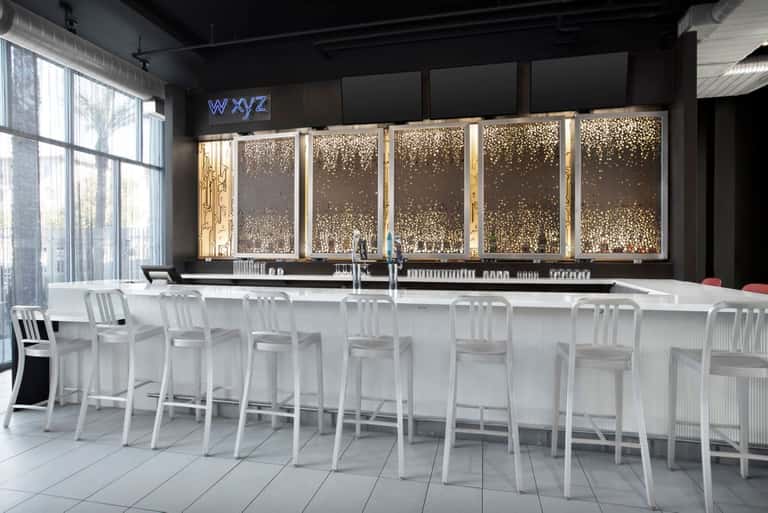 Contemporary hotel bar with white seating, illuminated decorative wall panels, and neon signage