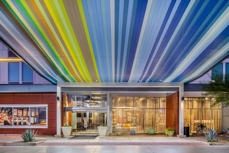 Colorful modern building entrance with vibrant rainbow striped canopy overhead and glass storefronts at dusk