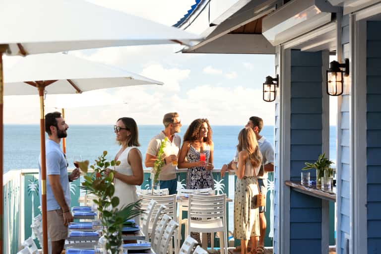 Group of guests socializing on a beachfront terrace with ocean views and white umbrellas