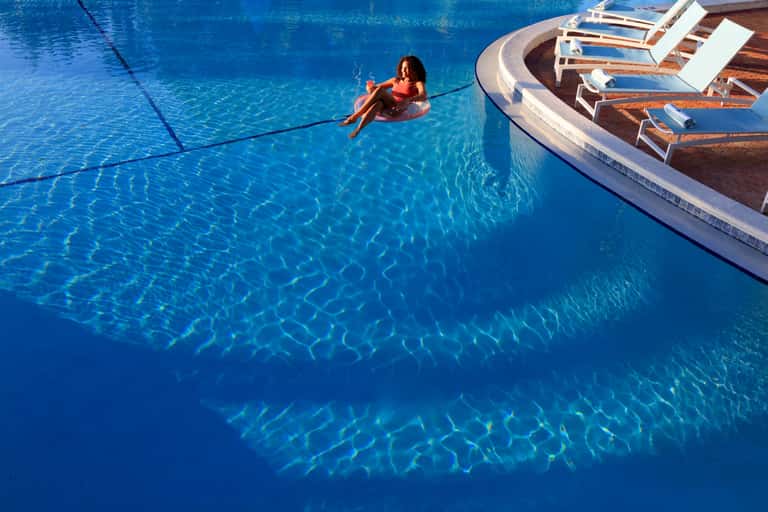 Woman swimming in a bright blue resort pool with lounge chairs poolside