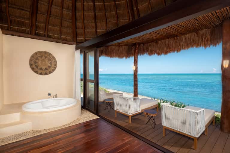 Luxury overwater villa bathroom with circular bathtub, ocean views, and thatched ceiling interior