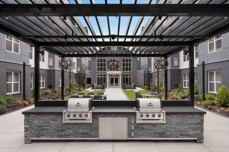 Outdoor covered patio with dual grills, stone countertop, pergola, and central courtyard with green lawn