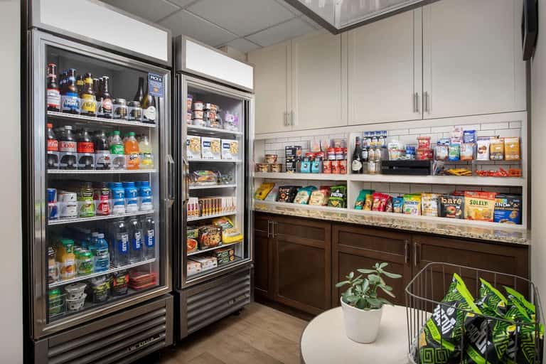 Hotel amenity pantry with refrigerated beverage coolers and stocked snack shelves