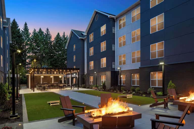 Residential complex courtyard at dusk with fire pit, cornhole, pool, and pergola seating area
