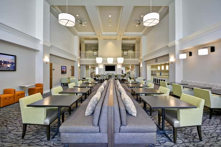Modern hotel lobby with high ceilings, gray seating islands, lime green armchairs, and elegant pendant lighting