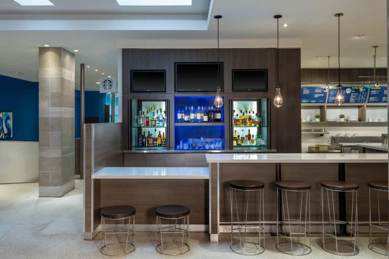Upscale bar with dark wood shelving, blue accent lighting, multiple television screens, and elegant cocktail seating